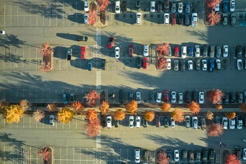 Aerial view of many colorful cars parked on parking lot with lines and markings for parking places and directions. Place for vehicles in front of a strip mall plaza