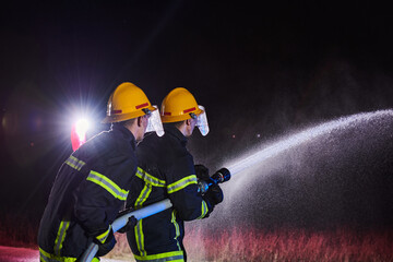 Firefighters using a water hose to eliminate a fire hazard. Team of female and male firemen in...