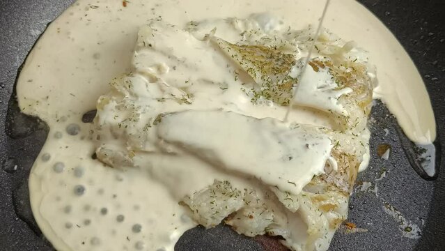 cr&egrave;me vers&eacute;e sur du filet de colin en cuisson, en gros plan, dans une po&ecirc;le	