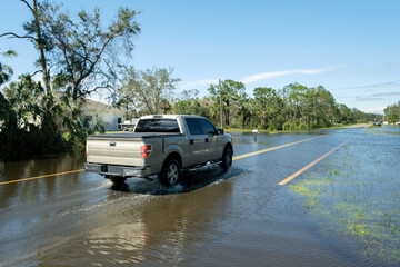 Flooded town street with moving cars submerged under water in Florida residential area after...