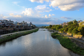 Obraz premium Kamo River, Kyoto, Japan | The River, Late Afternoon with Green Trees, Cloudy Sky, and Mountains in the Distance | Summer | July, 2023