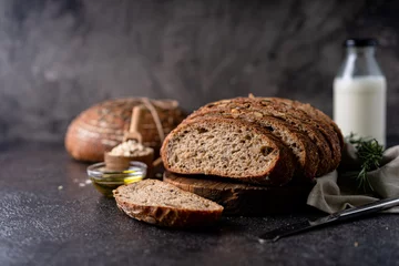 Rollo Brot Sliced sourdough bread from whole grain flour and pumpkin seeds on a grid, olive oil and black olive on a rustic wooden table. Artisan bread.  © ILHAM_PS
