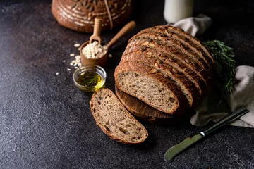 Fotobehang Sliced sourdough bread from whole grain flour and pumpkin seeds on a grid, olive oil and black olive on a rustic wooden table. Artisan bread. © ILHAM_PS