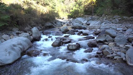 Closeup footage of a river stream flowing along big stones and green trees on a sunny day