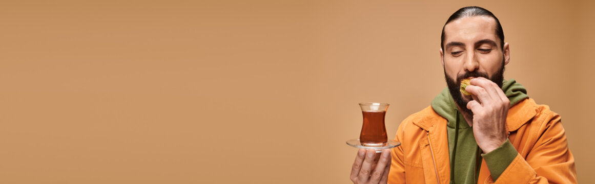 banner of happy bearded man holding turkish tea in traditional glass cup and eating tasty baklava