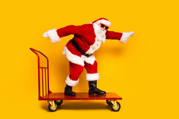 Full length profile photo of excited santa claus ride store pushcart empty space christmas offer isolated on yellow color background