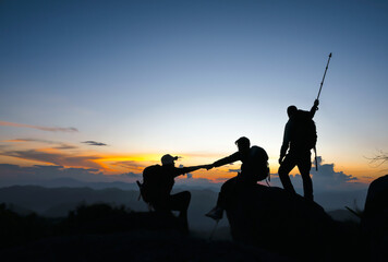 silhouette of group of mountaineers helping hands on top of mountains for successful hiking