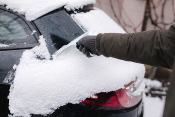 First person view of man cleaning snowy window on a car with snow scraper. Focus on the scraper....