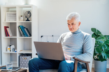 Professional Psychotherapy online. Middle aged male Psychologist having video call consultation on laptop while sitting on armchair In office. Specialist talking, counseling, helping patient online