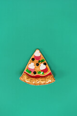 Merry Christmas food offers. Top view Artificial pizza slice decor on green background. Christmas background. Creative concept for seasonal and festive greetings for pizzeria and delivery service.