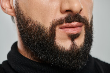 cropped shot of confident bearded arabic man in black turtleneck posing on grey background