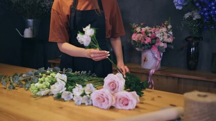 Hands of a female florist choosing flowers for a bouquet at her workplace in a flower shop. Close-up of a florist working.