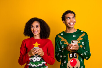 Photo of two cheerful creative people hold smart phone look curious empty space x-mas ad isolated...