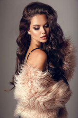 Beautiful winter woman portrait with long wavy hair and vogue style makeup in pink fur coat isolated on studio grey backround. Gorgeous chic girl model in sexy outfit.