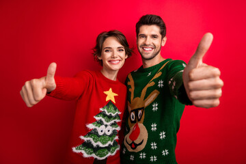 Photo of confident excited husband wife dressed ugly pullovers showing you thumbs up isolated red...