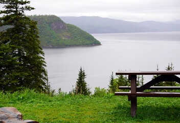 Picnic table overlooking a fjord in Gros Morne National Park with forested mountains in the...
