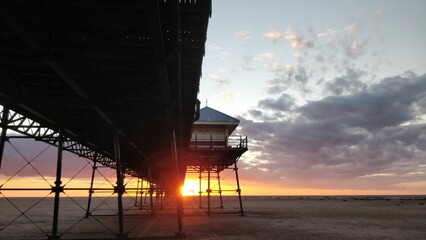 Beautiful view of a sunset at a sandy beach with a pier and a lifeguard tower