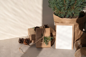 Crafted gift boxes, empty paper card mockup, juniper in pot on table with beige linen tablecloth,...
