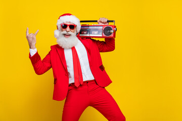 Fototapeta na wymiar Portrait of overjoyed funky grandfather demonstrate heavy metal symbol hold boombox x-mas eve isolated on yellow color background