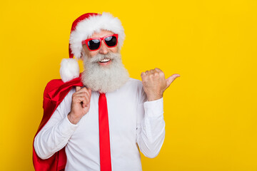 Photo of funny sweet retired man dressed xmas suit dark eyewear pointing thumb empty space isolated...