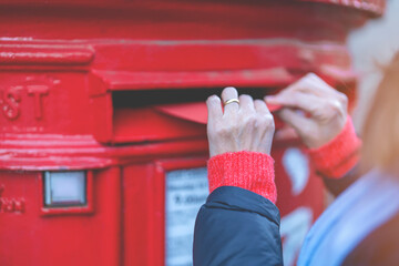 woman putting a card to red postbox and walking around English city - obrazy, fototapety, plakaty
