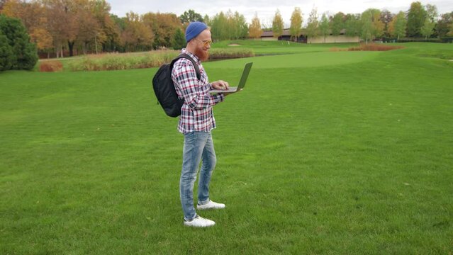 Spectacular autumn landscape with green lawn, distant yellow, orange and red trees. Happy traveller uses laptop for orienting himself in unfamiliar area. High quality 4k footage