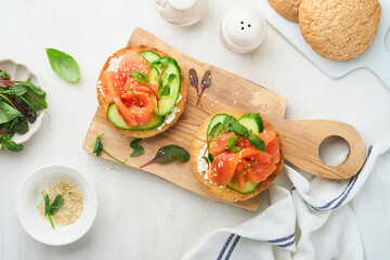 Open smoked salmon sandwiches with cream cheese, cucumber, sesame seeds, microgreens, spinach, and peas leaves on light old wooden background. Healthy breakfast food. Delicious snack. Top view.