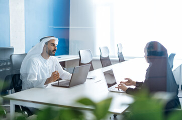 Man and woman with traditional clothes working in a business office of Dubai. Portraits of ...