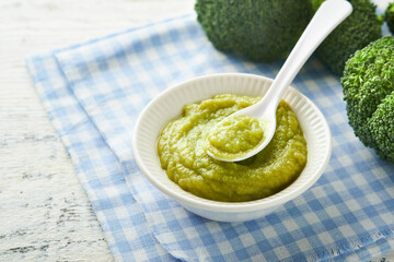 Green broccoli baby food in white bowl and jar on table. Green baby food. Child first feeding...
