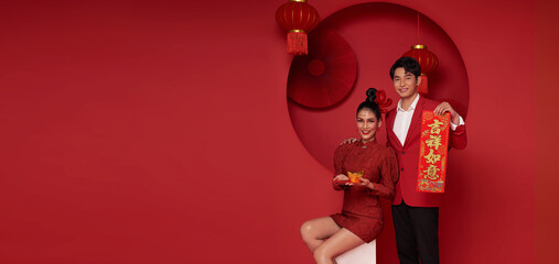 Happy asian couple in red casual attire holding angpao or red packet monetary gift and gold ingot...