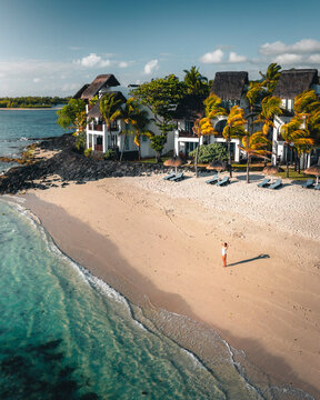 Aerial view of a woman on a luxury resort private beach along the shore with umbrellas at sunset, Ilot Lievres, Trou d'Eau Douce, Flacq district, Mauritius.