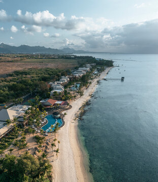 Aerial view of hotels and resorts on the beachfront along the coastline facing the ocean at sunset in Pointe aux Piments, Pamplemousses, Mauritius.
