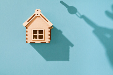 Concept of buying a house, a wooden house on a blue background, the shadow of a hand with keys.