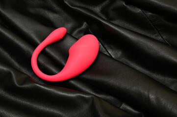 Pink dildo for women on the background of a black leather product. A vaginal simulator, a toy for adults.