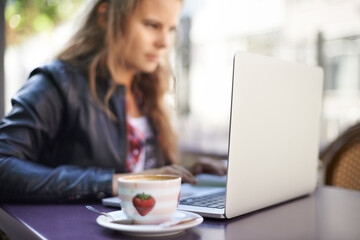 College student, working and laptop outdoor at coffee shop, cafe or restaurant with espresso, latte...