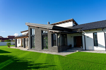 Fototapeta na wymiar Modern house with gray stone wall and white walls in a garden witg fresh green gras