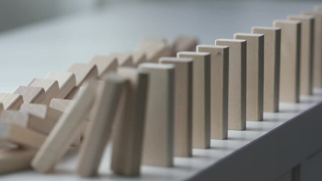 falling line of wooden domino blocks each knocking the next over, domino effect slow motion