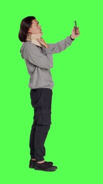 Profile of guy having cervical neck brace makes phone call informing family about his vertebral fracture injury. Full body greenscreen of wounded man wearing medical foam collar, speaking on telephone