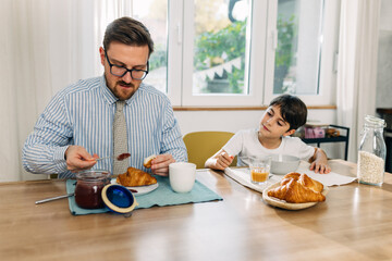 Boy is watching his father putting jam on pastry.