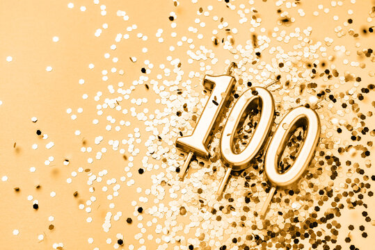 100 years celebration festive background made with golden candles in the form of number Hundred lying on sparkles. Universal holiday banner with copy space.
