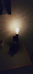 Vertical shot of an illuminated vintage light bulb on a small bedside table in a dark room