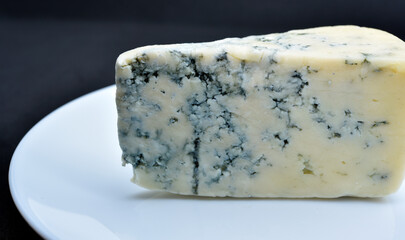 A piece of cheese with blue mold on a white plate. Delicious cheese.