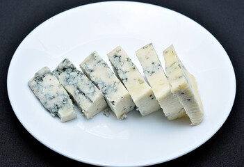 Sliced cheese with blue mold on a white plate. Delicious breakfast with cheese.