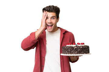 Young caucasian man holding birthday cake over isolated background with surprise and shocked facial...