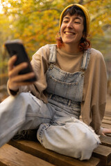 Woman with mobile phone and headphones in forest wearing yellow hat, listening to music, taking photos and video call