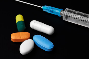 medical plastic syringe with colored tablets on a dark background