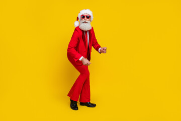 Fototapeta na wymiar Full length photo of positive handsome man pensioner dressed red suit santa hat smiling dancing isolated yellow color background