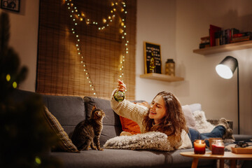 Cozy at home with tabby cat, woman playing with her kitten pet on sofa ay home in evening