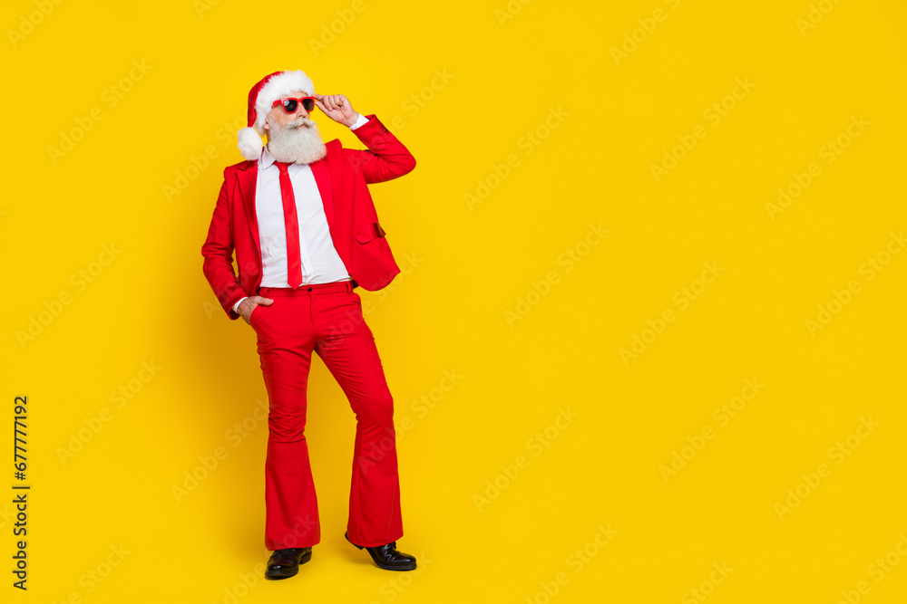 Poster full length photo of cool handsome man pensioner dressed red suit santa hat looking empty space isol