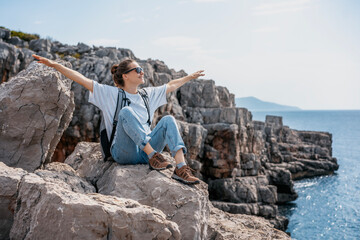 Woman traveler hiker relaxing on rocky seashore enjoying the view. Solo travel concept